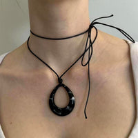 Black teardrop pendant choker necklace with adjustable tie cord, Y2K statement jewelry close-up, minimalist black pendant on cord choker, trendy IT girl aesthetic accessory, layered wrap choker necklace on neckline