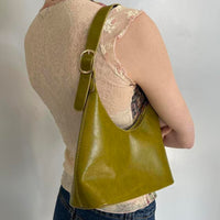 Back view of an olive green faux leather shoulder bag with adjustable buckle strap, styled on model. Minimalist Y2K hobo purse featuring a sleek silhouette, zip-top closure, and vintage-inspired design. Trendy olive handbag perfect for everyday wear, clean girl aesthetic, quiet luxury fashion, minimalist outfits, and modern it-girl style.