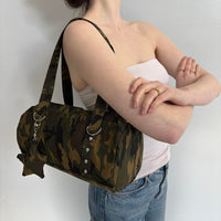 Y2K camouflage shoulder bag with silver hardware and charm detail, styled with a white tube top and denim jeans. Vintage-inspired camo purse featuring a spacious canvas design, trendy streetwear aesthetic, and army green camouflage print. Perfect everyday handbag for Y2K fashion, grunge outfits, Pinterest