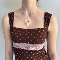Close-up of a brown polka dot lace tank top featuring a square neckline, blush pink floral lace panel, and fitted silhouette. Feminine coquette-inspired Y2K cami styled with a mother of pearl circle pendant necklace, perfect for soft girl outfits, vintage-inspired fashion, romantic aesthetic clothing, and Pinterest-worthy everyday looks.