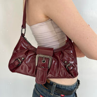 Close-up of burgundy faux leather Y2K shoulder bag on model, vintage-inspired cherry red handbag with silver buckle hardware, trendy slouchy shoulder purse, aesthetic 2000s IT girl bag, everyday streetwear accessory, minimalist faux leather handbag for going-out outfits and casual styling