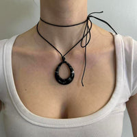 Black teardrop pendant choker necklace with adjustable tie cord, Y2K minimalist statement jewelry worn with white scoop neck top, trendy IT girl aesthetic, layered cord choker detail, modern edgy fashion accessory