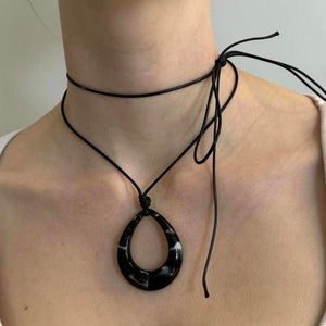 Black teardrop pendant choker necklace with adjustable tie cord, Y2K minimalist statement jewelry close-up, glossy black drop pendant on layered wrap choker, trendy IT girl aesthetic accessory on neckline