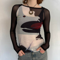 Close-up front view of black sheer mesh graphic top for women with long sleeves, fitted stretchy Y2K going out top, abstract print cool girl blouse, trendy boutique fashion shirt paired with denim jeans, sheer streetwear top.