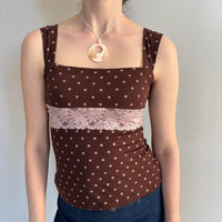 Brown polka dot lace tank top with pink floral lace trim, square neckline, and adjustable tie-back detail. Feminine coquette-inspired Y2K cami top styled with a mother of pearl pendant necklace, perfect for soft girl, vintage-inspired, and Pinterest aesthetic outfits.