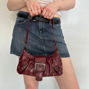 Burgundy faux leather shoulder bag styled with denim mini skirt, vintage-inspired Y2K handbag with silver buckle hardware, trendy cherry red slouchy purse, aesthetic 2000s IT girl accessory, everyday shoulder bag for streetwear, casual outfits, and going-out fashion looks