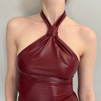 Close-up of a women’s burgundy vegan leather halter top with a twisted neck detail, body-hugging fit, glossy faux leather fabric, trendy clubwear style, dark feminine aesthetic, and Y2K-inspired fashion top.