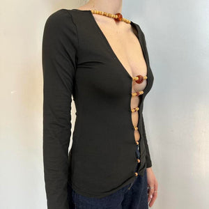 Side view of black beaded cutout long sleeve top for women with deep plunge neckline, stretchy fitted Y2K going out top, trendy boutique fashion shirt with wooden bead front detail, sexy black night out top styled with jeans.