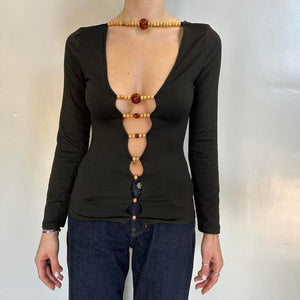 Front view of black beaded cutout long sleeve top for women with deep plunge neckline, stretchy fitted Y2K going out top, trendy boutique fashion shirt with wooden bead front detail, sexy black night out top paired with jeans.