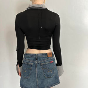 Back view of black and grey office siren contrast collared top for women with long sleeves, fitted stretchy Y2K crop top, corporate chic blouse with cuffed sleeves and open back tie detail, trendy boutique fashion top paired with denim mini skirt.