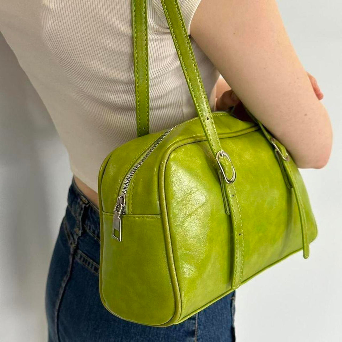 Lime green Y2K shoulder bag close-up, glossy faux leather mini baguette purse with zipper detail and adjustable buckle straps, vintage-inspired 2000s handbag, trendy retro aesthetic accessory styled with white ribbed top and denim, statement mini shoulder bag for women