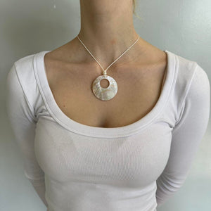Mother of pearl shell pendant necklace with iridescent circular charm on a minimalist white cord chain, styled with a fitted white ribbed top. Trendy coastal jewelry inspired by clean girl fashion, Y2K aesthetics, Pinterest outfits, and beachy minimalist style.