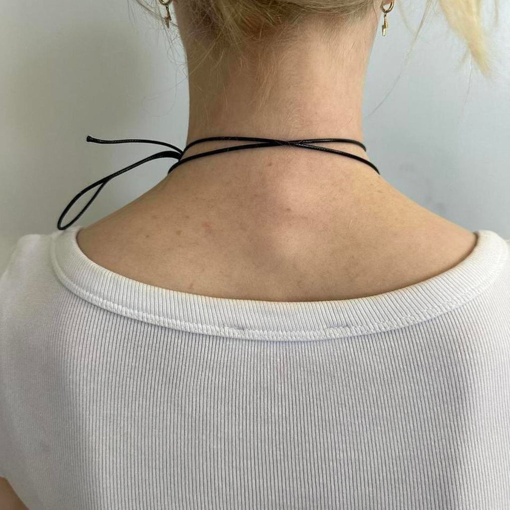 Back view of black adjustable tie choker necklace, thin cord Y2K minimalist jewelry, wrap-around choker tied at neck, trendy IT girl aesthetic accessory styled with white ribbed top
