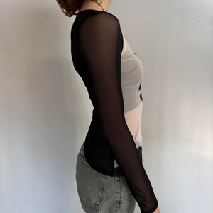 Side view of black sheer mesh graphic top for women with long sleeves, fitted stretchy Y2K going out top, abstract print cool girl blouse, trendy boutique fashion shirt with sheer sleeves paired with denim jeans.