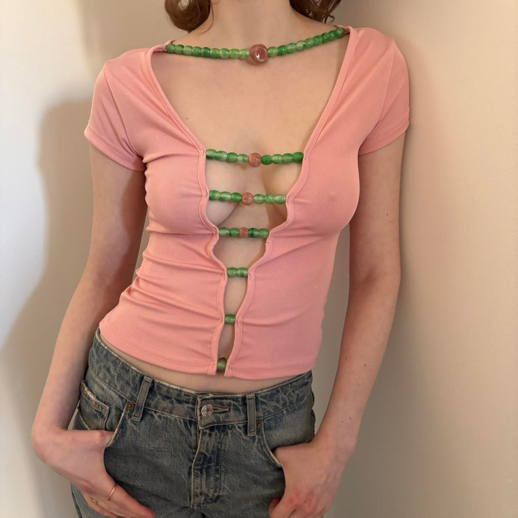 Front angled view of pink beaded cutout top for women, Y2K aesthetic baby tee with green bead detailing, stretchy fitted short sleeve crop top, trendy coquette style outfit paired with low rise denim jeans, boutique fashion statement piece.