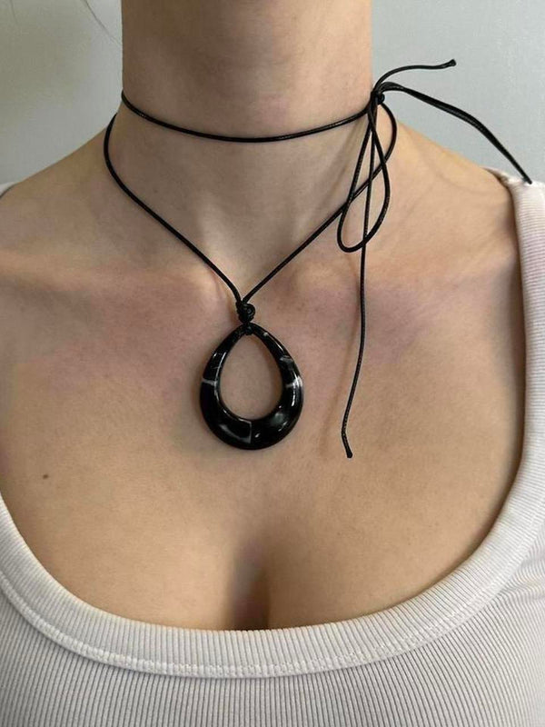 Black teardrop pendant choker necklace with adjustable tie cord, Y2K minimalist statement jewelry worn with white scoop neck top, trendy IT girl aesthetic, layered cord choker detail, modern edgy fashion accessory