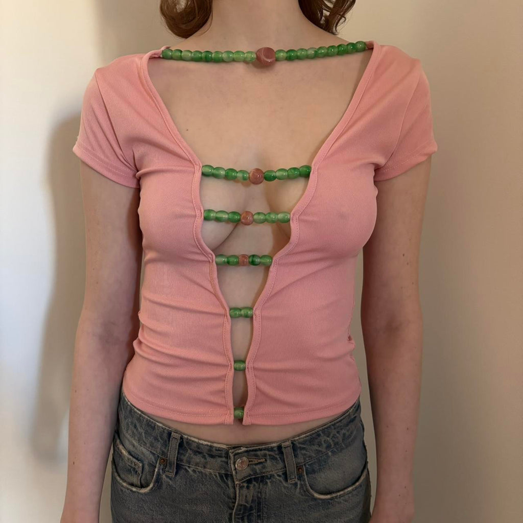 Front view of pink beaded cutout top for women, Y2K aesthetic baby tee with green bead detailing, stretchy fitted short sleeve crop top, trendy coquette style summer outfit paired with low rise denim jeans, boutique fashion statement top.