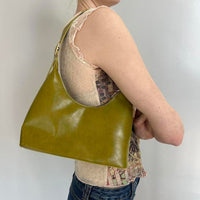Olive green faux leather shoulder bag styled on model, featuring a sleek minimalist silhouette and Y2K-inspired design. Trendy olive handbag perfect for everyday wear, casual outfits, vintage fashion, clean girl aesthetic, minimalist style, and modern it-girl wardrobes. Spacious hobo purse with a chic underarm fit and timeless fashion appeal.