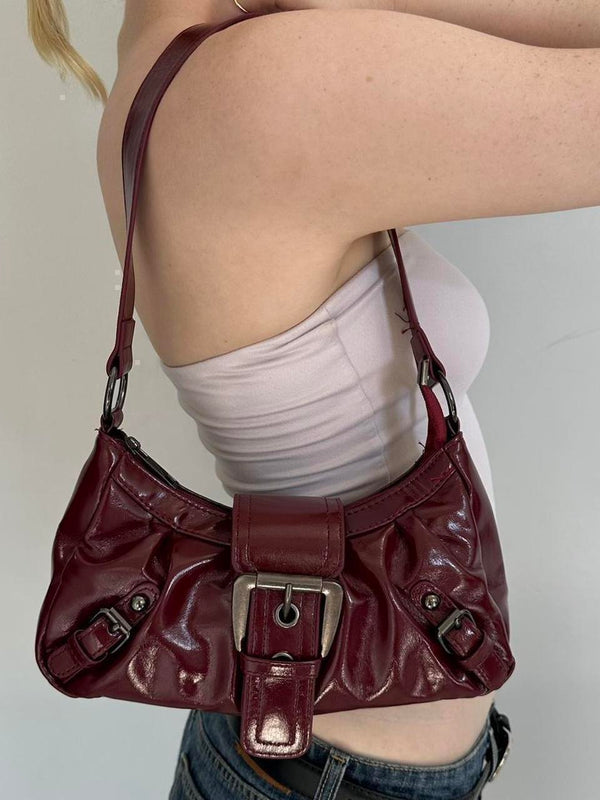 Burgundy faux leather shoulder bag styled on model, vintage-inspired Y2K handbag with silver buckle detail, trendy cherry red purse, slouchy 2000s shoulder bag, aesthetic IT girl accessory, everyday faux leather handbag for streetwear and going-out outfits