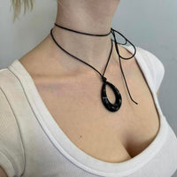 Black teardrop pendant choker necklace with adjustable tie cord, Y2K minimalist statement jewelry, layered wrap choker on neckline, glossy black pendant detail, trendy IT girl aesthetic accessory styled with white ribbed top