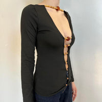 Side view of black beaded cutout long sleeve top for women with deep plunge neckline, stretchy fitted Y2K going out top, trendy boutique fashion shirt with wooden bead front detail, sexy black night out top styled with jeans.